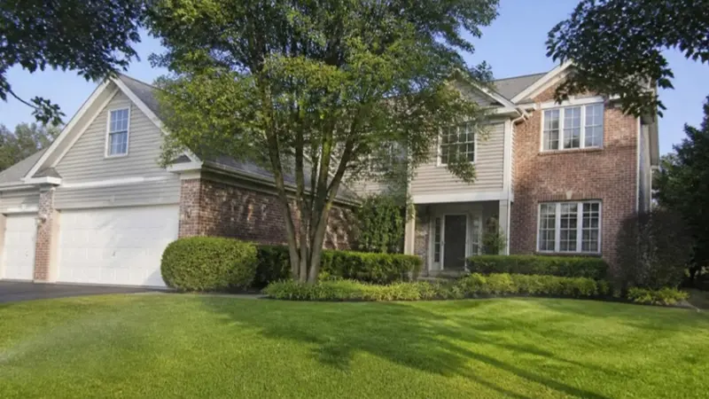 1990s-style two-story brick home with mature landscaping and a green front lawn